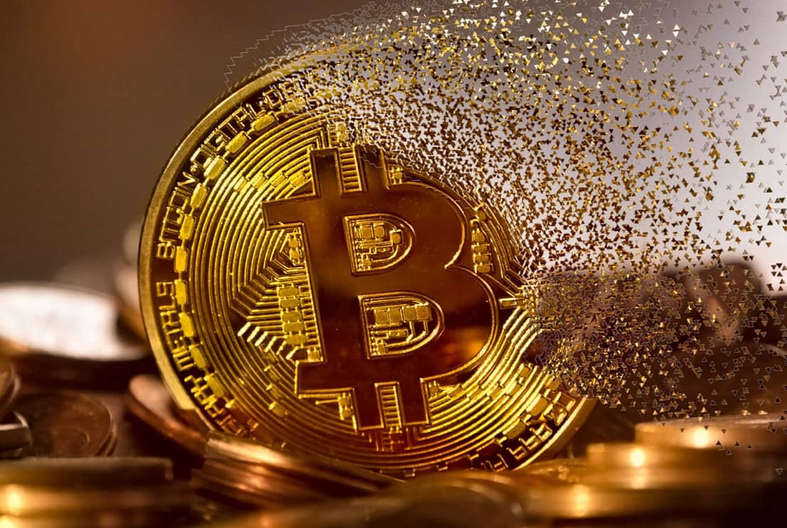 A Bitcoin coin disintegrating into small particles on the right side