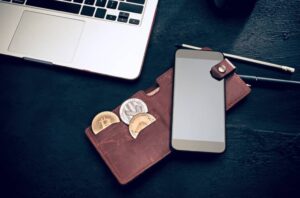 A laptop, a wallet with coins, and a phone on a dark surface